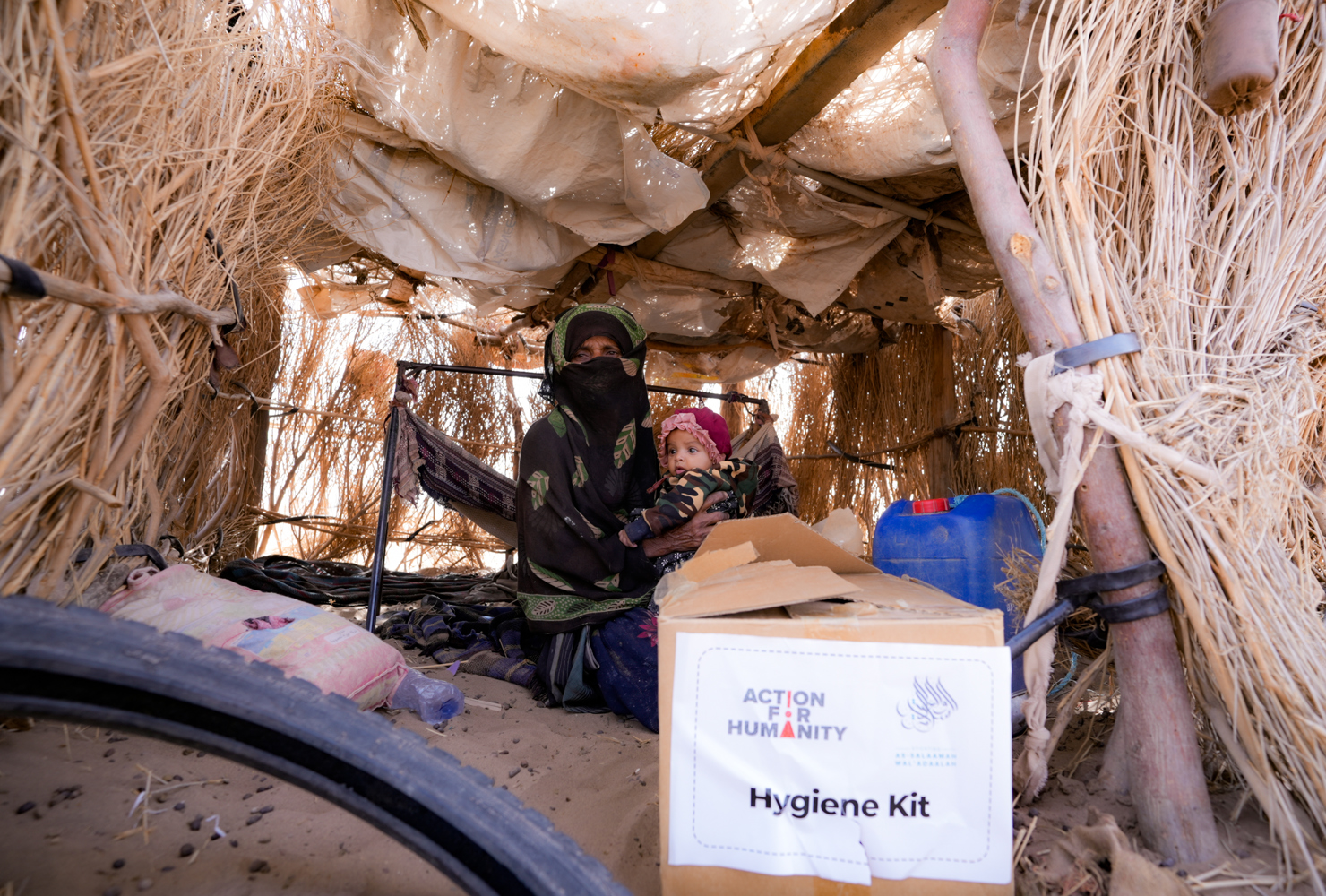 70 year old Hadara tends to her grandchild in 28°C heat with little protection from the sun or sand sweeping wind